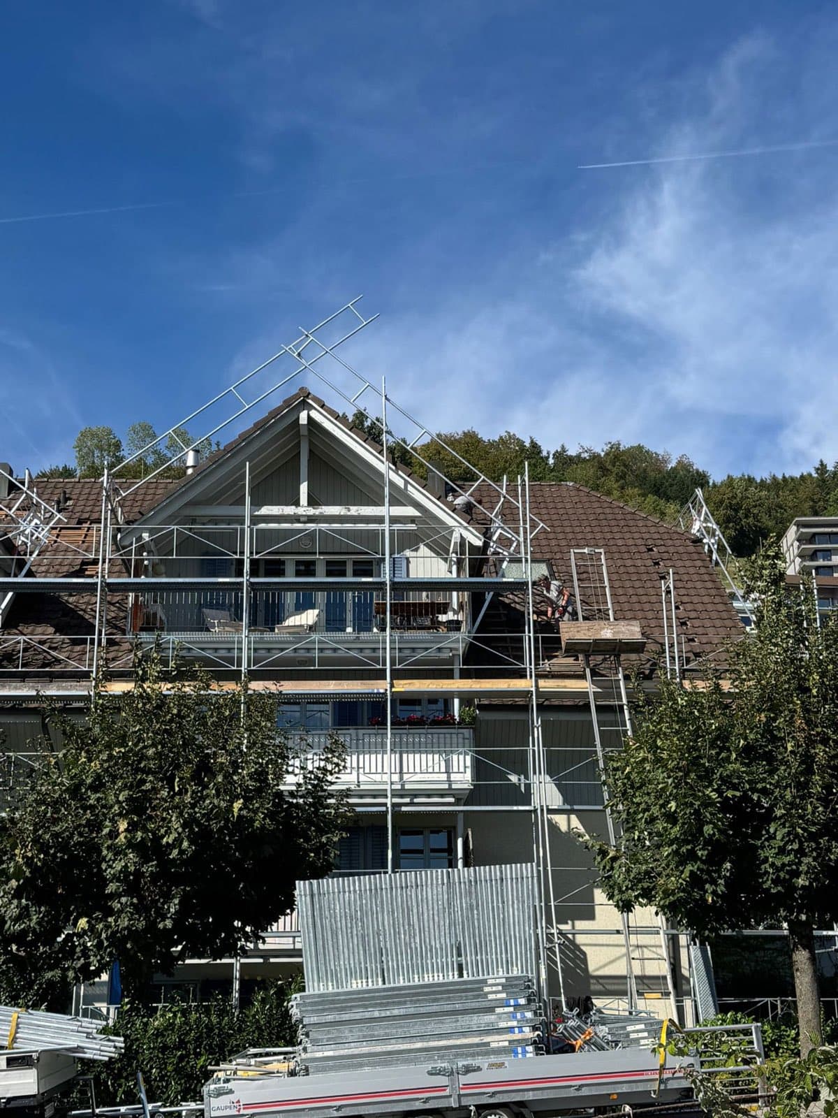 Fangwand eines Dachfanggerüsts am Giebel eines Mehrfamilienhauses, Monteur bei der Arbeit auf dem Ziegeldach