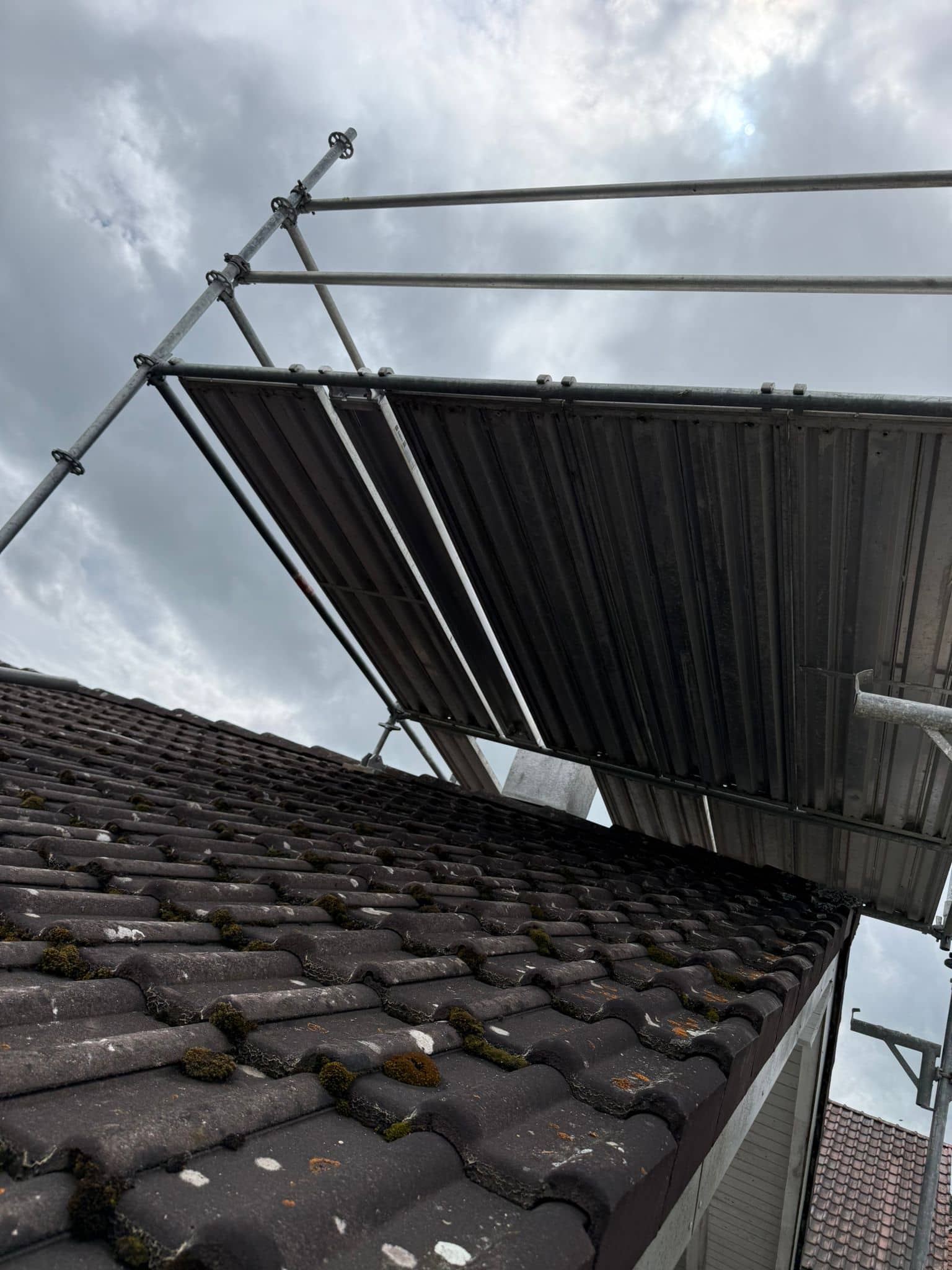 Modulgerüst der Elian Gerüstbau GmbH mit Dachschutzwand und Konsolen über einem Ziegeldach in der Schweiz